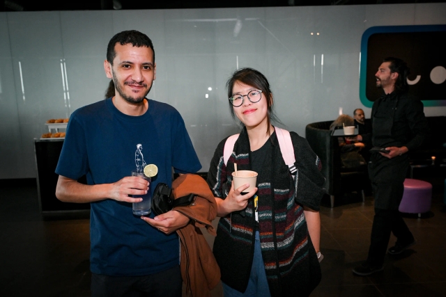 A man holding a purple cocktail poses with a woman holding an appetizer. 