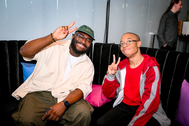 Darius, core contributor, poses in the lounge with a guest. Both men are holding up peace signs.