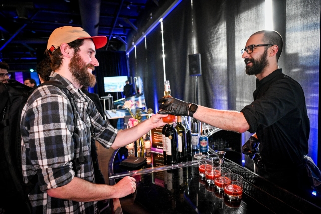 A bearded guest with a cap receiving their drink at the alcohol bar.