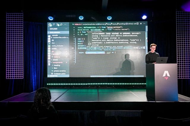 Ben Holmes on stage at the podium, sharing a demo. He is live-coding.