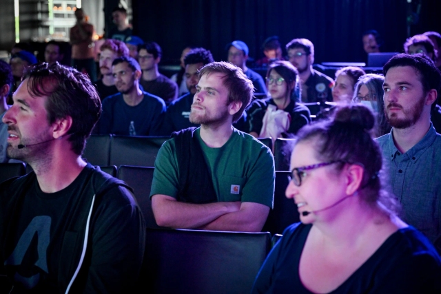 A shot of an audience member, listening to the keynote speaker intently with his arms crossed.