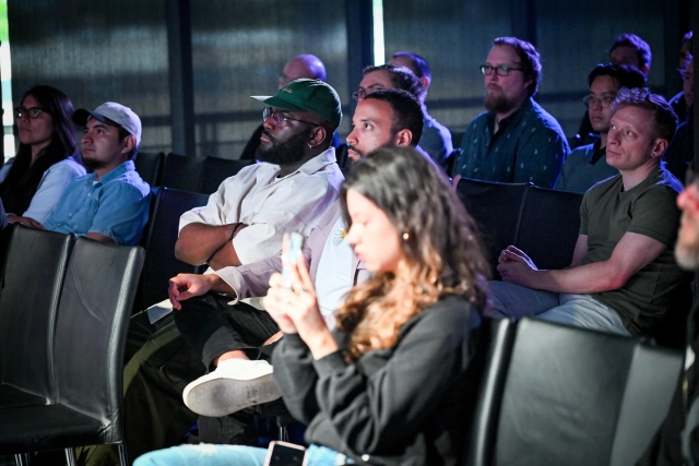 Audience members listening to Fred K. Schott speak on stage. A woman holds up her phone, filming social media content of the keynote.