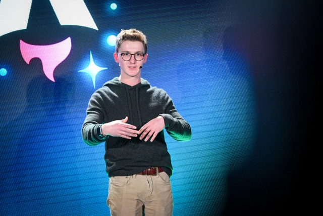 Closeup of Ben Holmes on stage with his hands together, answering a question from the audience.