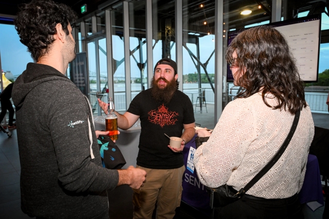 Guests chat in front of floor-to-ceiling windows while holding their food and drink.