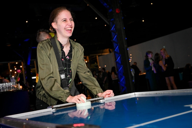 A guest smiles brightly as they play air hockey.